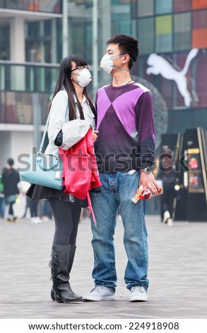 BEIJING-OCT. 19, 2014. Young face masked Chinese couple. Beijing raised its smog alert to orange because the air quality is a health threat. Face masks, once a rarity in Beijing, have become common.