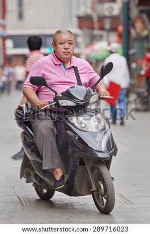 BEIJING, CHINA -JUNE 9, 2015. Overweight man on an e-bike. China\'s obesity rate has skyrocketed over the last three decades, resulting in 46 million obese Chinese adults and 300 million who are overweight.