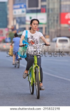 BEIJING-JULY 10, 2015. Young woman rides a public share bicycle. Bicycle sharing allow to hire on a very short term basis, it is a very popular transport mode among commuters in major Chinese cities.