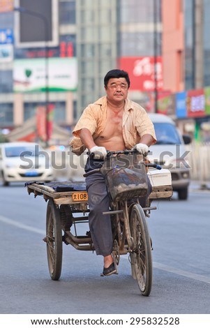 BEIJING-JULY 10, 2015. Man on rusty three wheeled freight bike. Although municipal governments try to ban them out this transportation mode is still convenient in dense, congested Chinese cities.