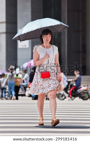 KUNMING-JULY 5, 2014. Chinese girl with an umbrella as sun blocker. Since ancient times a pale skin is an absolute Chinese beauty ideal. A tanned skin is often associated with low class workers.