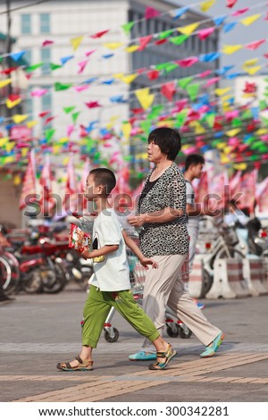BEIJING-JULY 24, 2015. Female elder with grandson in shopping area. In order to help their children pursue professional goals, older Chinese people often take an active role in raising grandchildren.