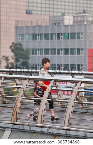BEIJING-JULY 27, 2015. Elder woman with granddaughter on pedestrian bridge. In order to help their children pursue professional goals, older Chinese often take an active role in raising grandchildren