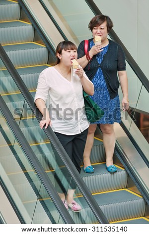 BEIJING-AUGUST 19, 2015. Fat woman eat ice cream on escalator. China\'s obesity rate skyrocketed over last three decades, resulting in 46 million obese Chinese adults and 300 million who are overweight