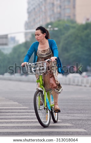 BEIJING-JULY 27, 2015. Elegant woman rides public share bicycle. Bicycle sharing allow to hire on a very short term basis, it is a very popular transport mode among commuters in major Chinese cities.