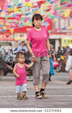 BEIJING-AUG. 5, 2015. Female elder with grandson in shopping area. In order to help their children pursue professional goals, older Chinese people often take an active role in raising grandchildren.