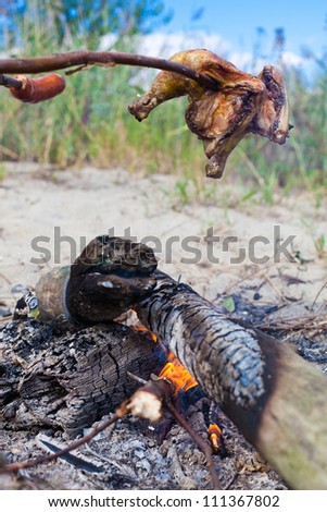 Roasting chicken meat and sausages on campfire