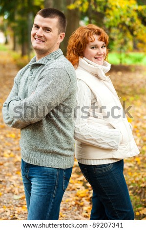 Happy couple standing back to back in autumn park