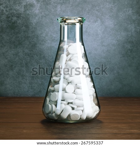 Chemical laboratory Erlenmeyer flask full of pills or tablets standing on wooden surface behind old grey wall background