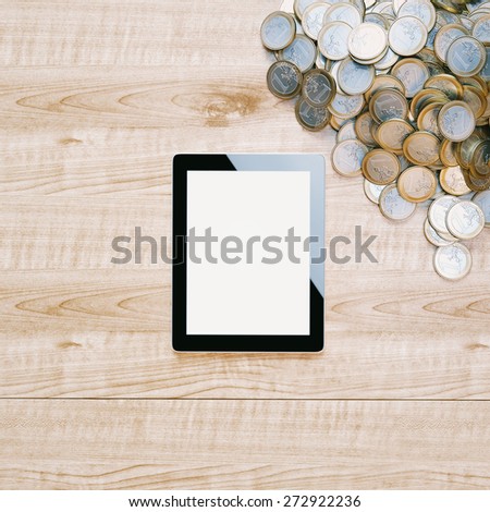 Pile of euro coins and touch screen tablet on wooden surface. Conceptual technology picture.