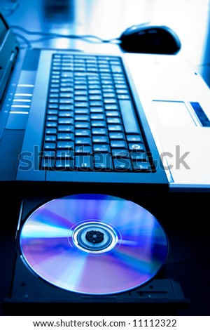 Laptop computer with opened cd-tray. Blue toned image, focus is on the disk.