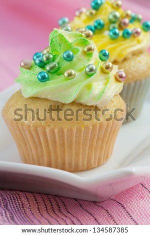 Two cupcakes  with yellow and green  butter cream and colorful decorations, on pink background