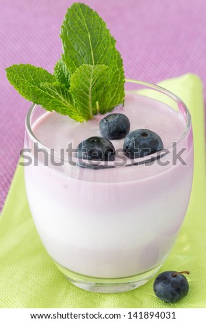 Single glass of fruit yogurt dessert with blueberries and mint decoration, on purple and green background