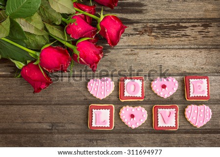 Red roses and pink cookies in shape of LOVE word, on wooden background, top view