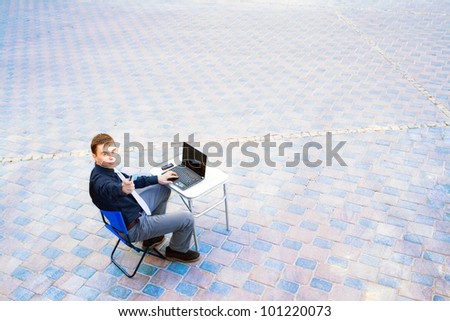 The image of a businessman working on the computer and sitting in the middle of the street