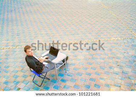 The image of a businessman sitting at the table in the street, which works with the computer and has a success.