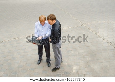 Image of the business partners using computer and standing on the street. They have absolutely thoughtful face.