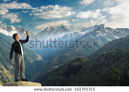 Image of a businessman standing on the top of the mountain, using a laptop, shouting because connection break. In the background a beautiful panorama of the valley with high peaks.