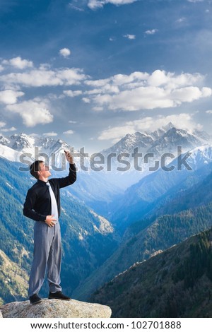 Image of a businessman standing on the top of the mountain, using a laptop, shouting because connection break. In the background a beautiful panorama of the valley with high peaks.