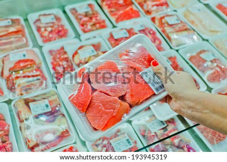 Image of packaged meat with woman hand in the supermarket