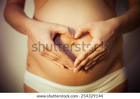 Pregnant woman holding her hands on her stomach in the form of heart