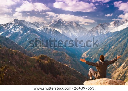 Image of a successful businessman, he sits on the top of mountains on the background