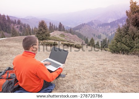 man dressed in red sweater uses laptop remotely with 3g or 4g network wireless at mountain, square orientation
