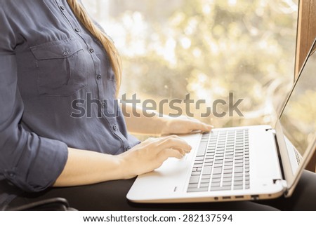 Beautiful happy student with a laptop sitting against a bright window. Young woman learn and using a computer connected to the network via wifi, 4g. Monochromatic color