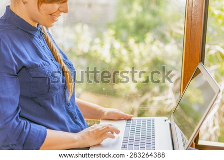 Beautiful happy student with a laptop sitting against a bright window. Young woman learn and using a computer connected to the network via wifi, 4g