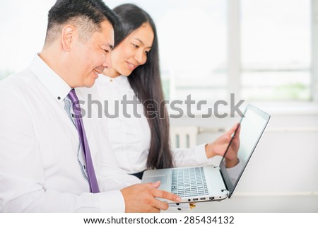 Asian business people dressed in white shirts analyze their work on the laptop at the office