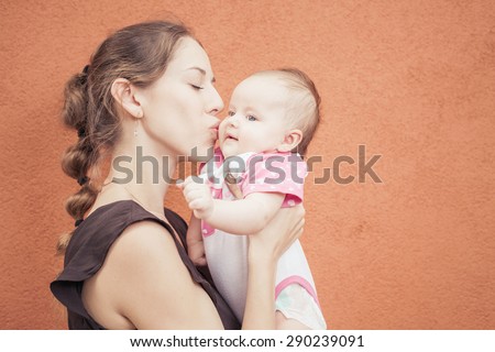 Happy mother kissing her baby at wall background. Mothercare is most important in baby life. Image ready for International Kissing Day or World Kiss Day 6 July, with copy space for any text