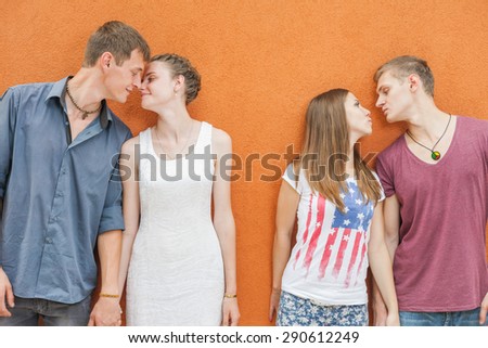 Small group of young people kissing and looking into eyes, they standing in row near red wall background. They celebrate a holiday of International, World Kissing Day 6 July or Valentine\'s Day