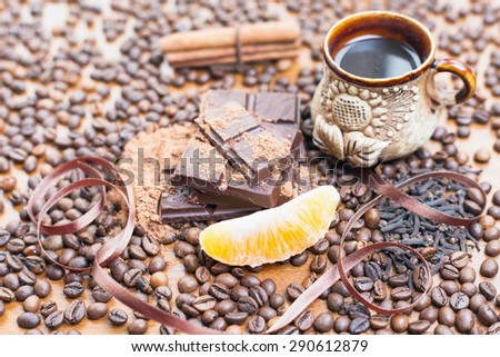 For holiday of chocolate day - wooden table background decorated a lot of coffee beans, chocolate bar, a cup of hot coffee, cacao, orange slice, cinnamon, clove