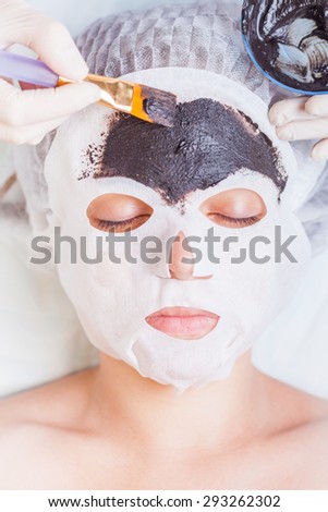 Cosmetologist in spa salon applying mud face mask using cosmetological brush. Concept of beauty, healthy therapy, rejuvenation, skincare and relaxing at luxury resort