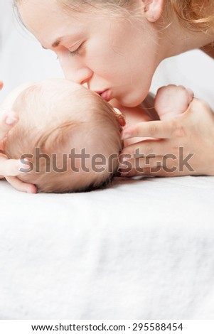 Newborn baby girl lying on a white bed and happy mother kissing a baby, with large copy space for any text. Mother care is most important in baby life
