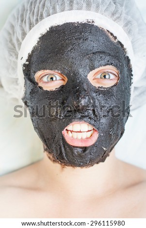 Woman in spa salon with black mud face mask, with bright emotions of crazy woman, surprise or creative idea came! Concept of beauty, healthy therapy, rejuvenation, skincare, relaxing at luxury resort