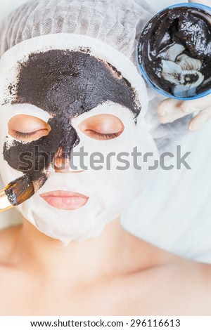 Cosmetologist in spa salon applying mud face mask using cosmetological brush. Concept of beauty, healthy therapy, rejuvenation, skincare and relaxing at luxury resort