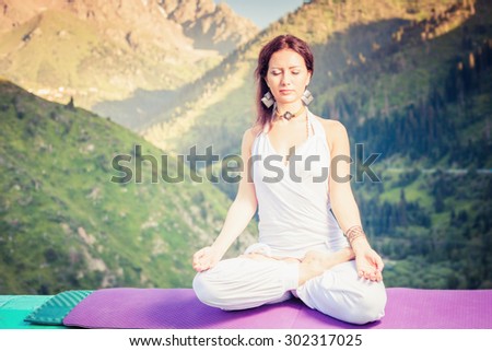 Beautiful woman relaxing and meditating outdoor at swiss mountain. She sits at peak of mountain in lotus position and feel harmony of your body and nature. Healthy lifestyles concept of body and soul