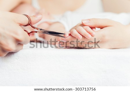 Mom tonsured nails on the hands newborn using nail scissors. Mother care is most important for baby healthy life. There is a copy space for any text