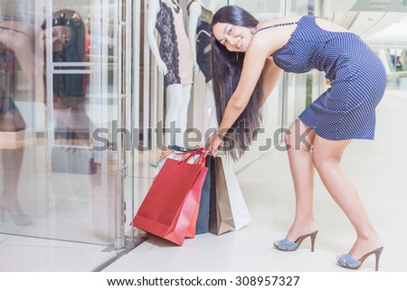 Fashion Asian woman pulls out a lot of bags with goods from a boutique at the big mall centre. Concept of shopping or shopaholic, sales and discounts at boutique