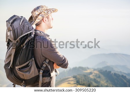 Climbing young adult at the top of summit with aerial view of mountain range. He dressed fashion heat and backpack