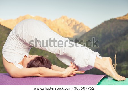 Beautiful woman doing difficult exercise of yoga outdoor at swiss mountain. She lies at peak of mountain and feel harmony of your body and nature. Healthy lifestyles concept of body and soul