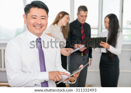 Executive asian boss using tablet pc with his successful business team at background. Multiracial people is a good addition for running a successful business