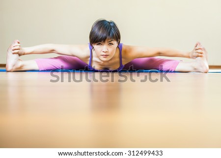 Asian woman doing splits for yoga exercise indoor at home. She looking at camera. Concept of healthy lifestyle with copy space for any text at foreground