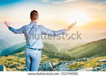 Image of a young businessman who sits on the top of the mountain and looks into the distance to the beautiful mountains, thinking about future plans