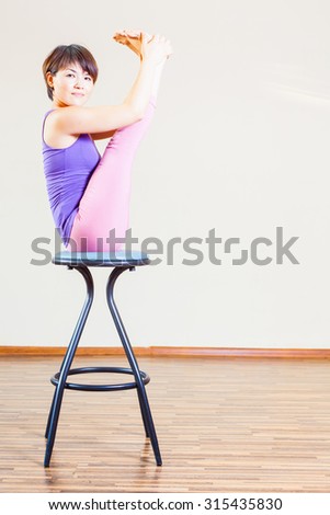 Asian woman doing exercise or yoga at her home at bar chair. You can maintain regular workouts at your home for free, be healthy and in good tonus!