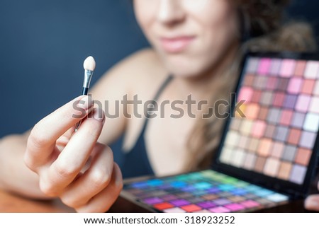 beautiful caucasian woman doing makeup using cosmetic brush applying eye shadow or foundation of makeup. Image at beauty salon with black background. Selective focus at brush