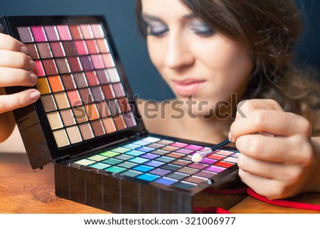beautiful caucasian woman doing makeup using cosmetic brush applying eyeshadow or foundation of makeup. Image at beauty salon with black background. Selective focus at brush