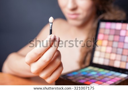 beautiful caucasian woman doing makeup using cosmetic brush applying eye shadow or foundation of makeup. Image at beauty salon with black background. Selective focus at brush