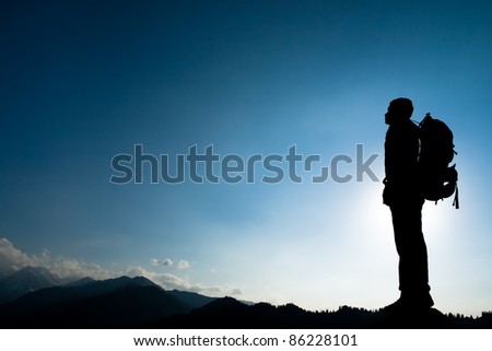 Silhouette of climbing young adult at the top of summit with aerial view of the blue sky